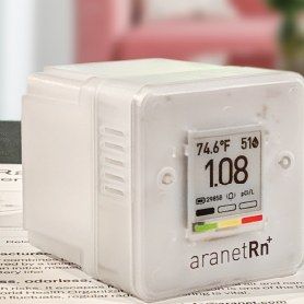 The Aranet RN+ radon monitor, a white cube with an e-ink display, on a table.