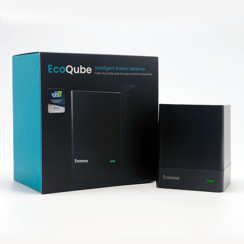The Ecosense EcoQube radon monitor, a small black cube, beside its box.