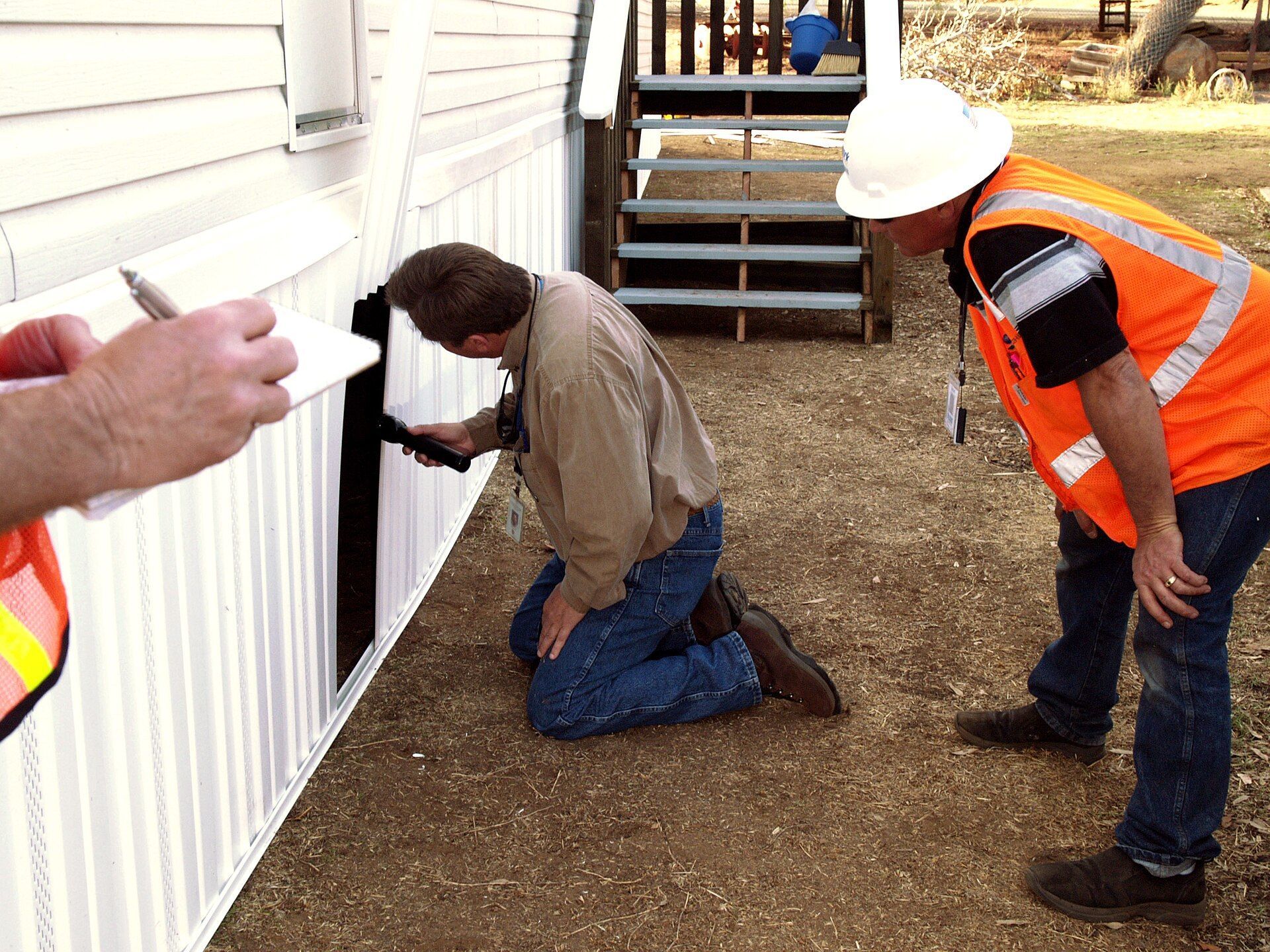 A building inspector checking a wall inside a house while another man watches.