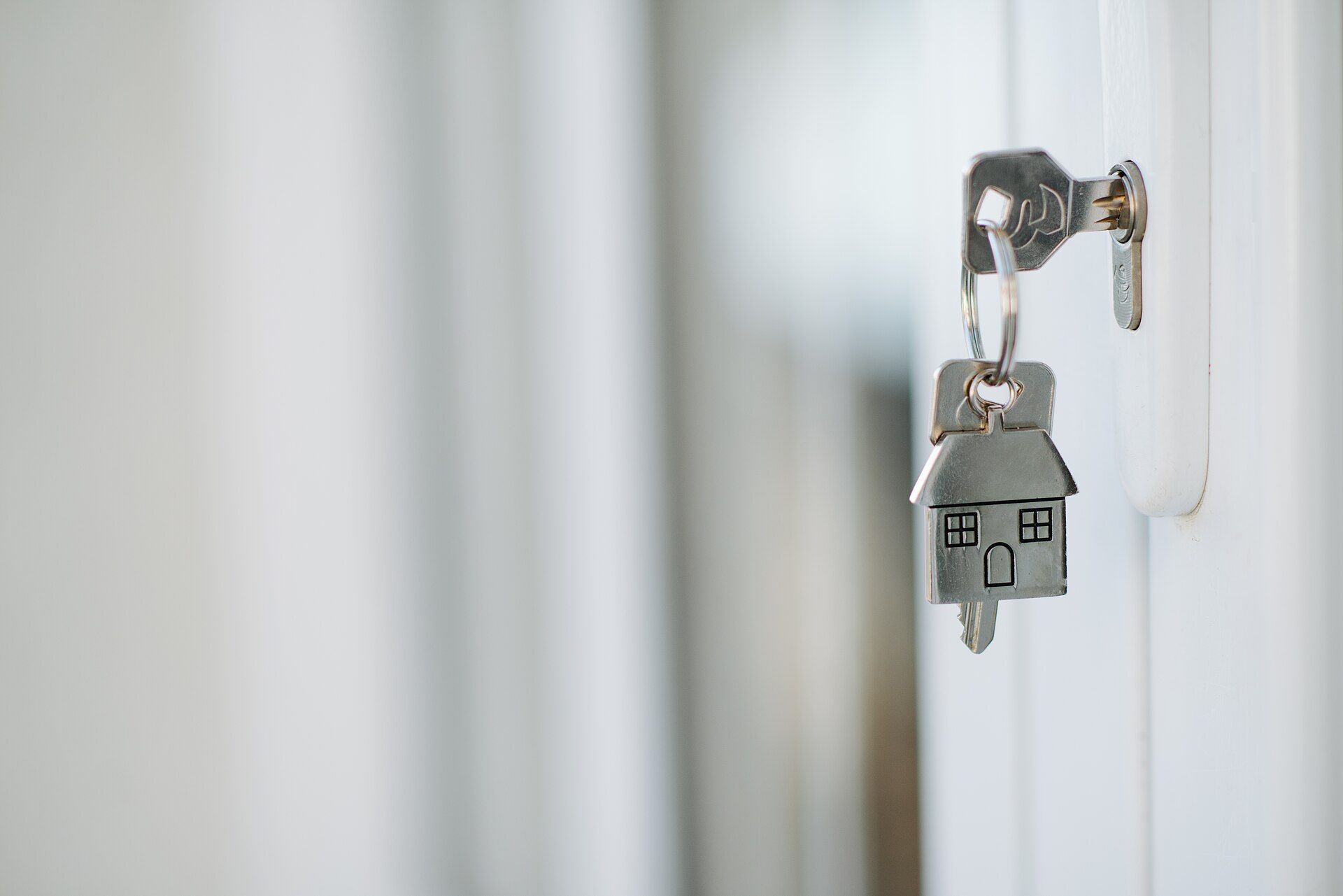 A key with a small house keychain in a door lock.