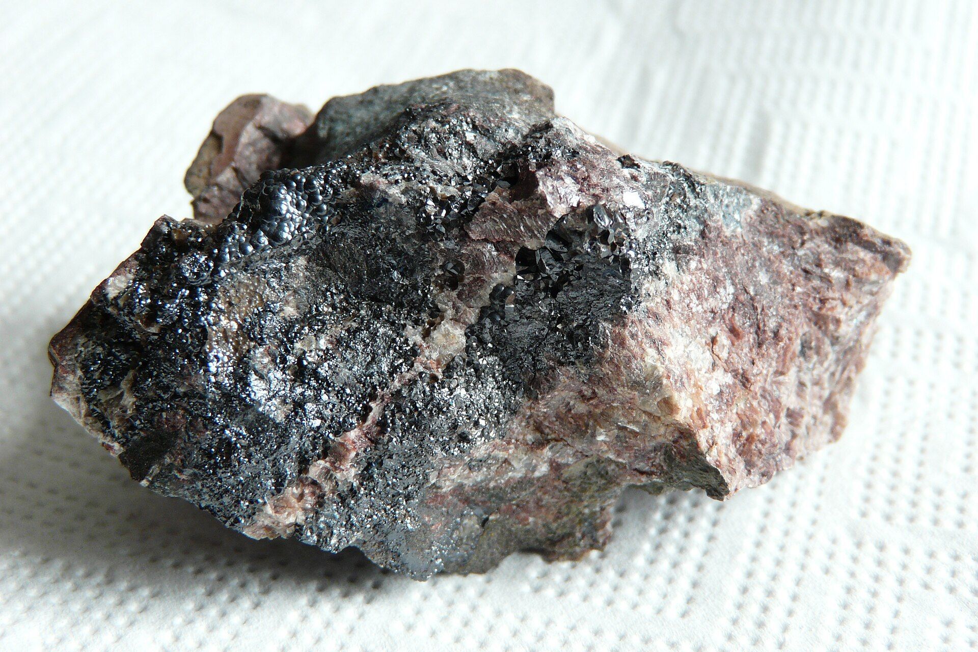 A piece of uraninite, a dark uranium mineral, on a white background.